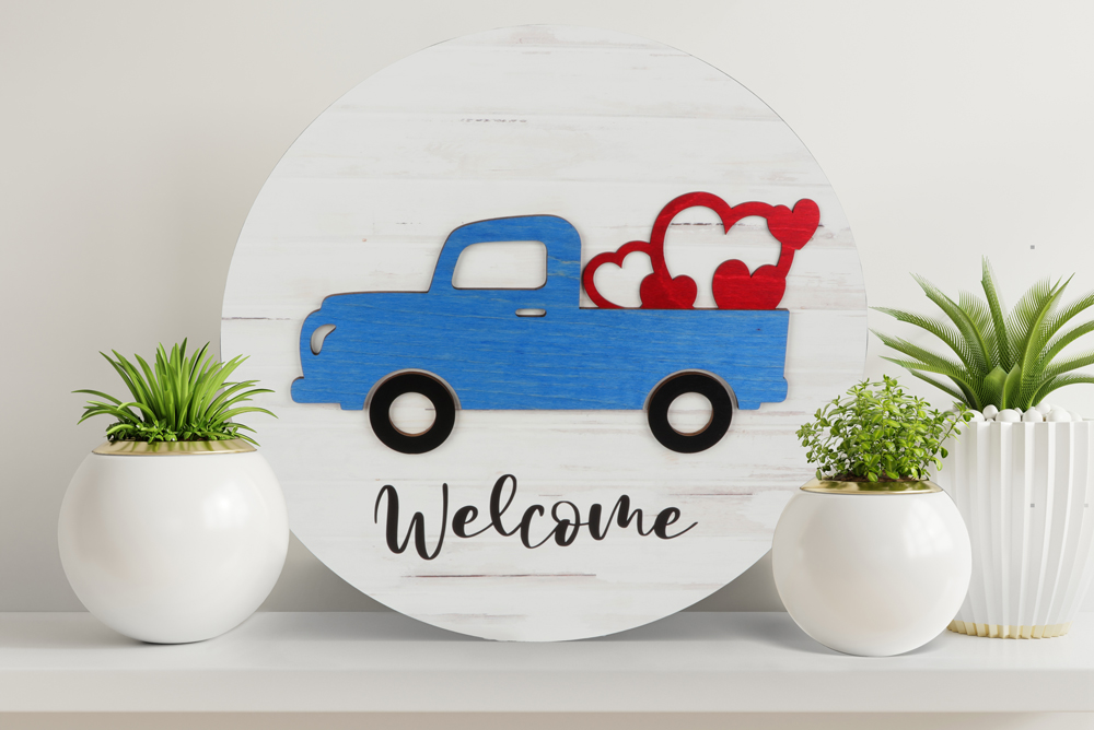 Wooden round wall hanging with hearts in the back of a truck that says Welcome