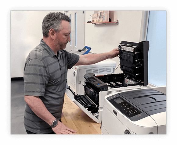 man working on one of three printers on a table