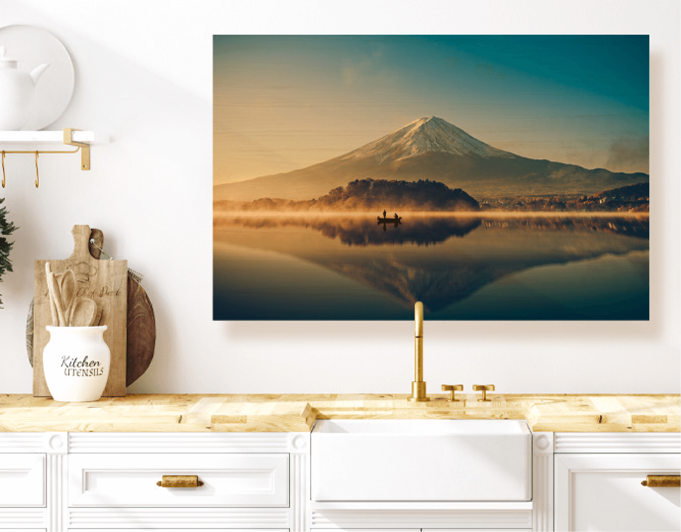 Picture of a mountain reflecting on a lake is hung on the wall behind a kitchen sink, canister of kitchen utensils displayed on the counter