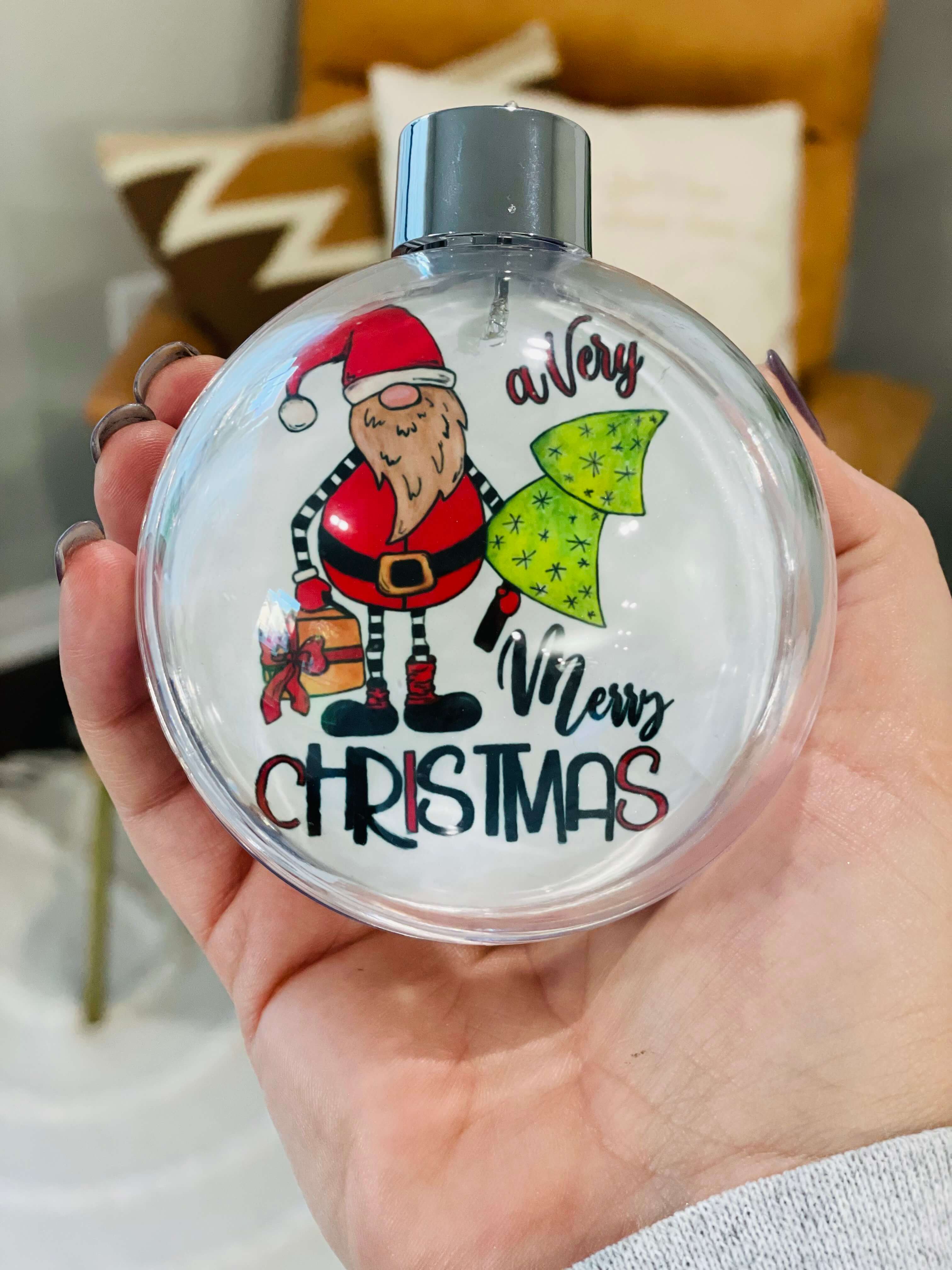 Hanging ball ornament with "Merry Christmas" under a santa holding a tree