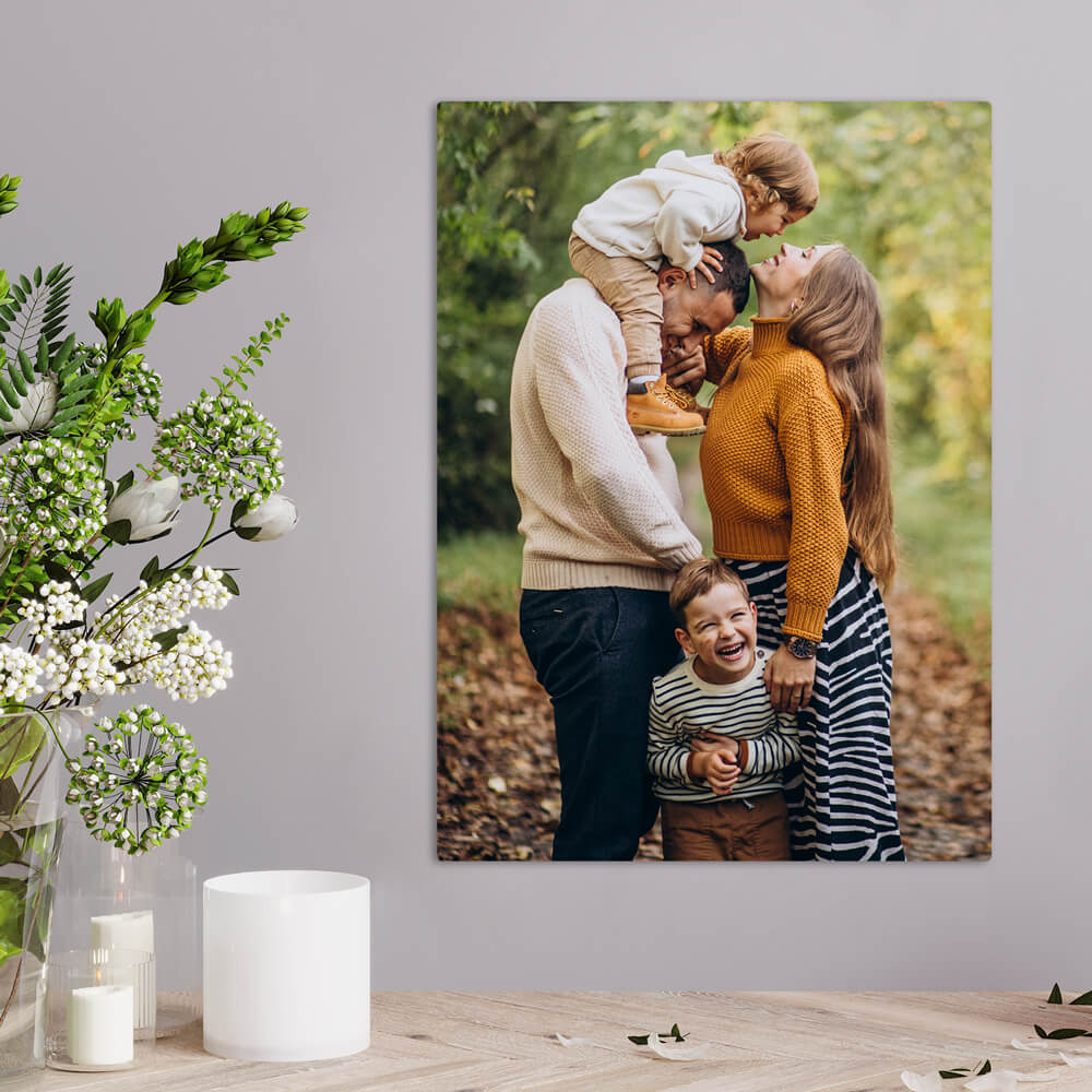 Family photo of parents with two children hung on the wall near candles and a flower vase.